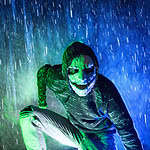 Masked character at Factory of Terror Haunted House in the rain with eerie blue and green lighting.