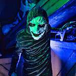 Masked character at Factory of Terror Haunted House with green and blue lighting.