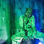 Spooky character at Factory of Terror Haunted House with green and blue lighting.