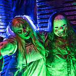 Two spooky characters at Factory of Terror Haunted House with eerie green and blue lighting