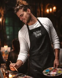 Guest painting at Factory of Terror Paint Night wearing branded apron in a candlelit haunted house setting
